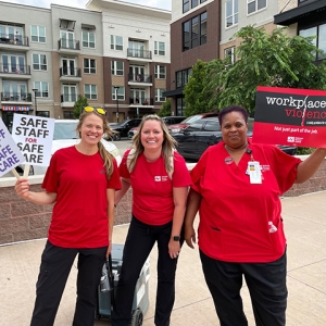 Three nurses outside smiling holding signs calling for safe staffing and workplace violence prevention