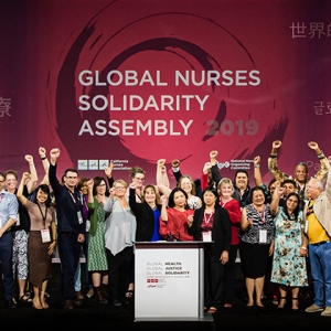 Large group of nurses on stage in front of banner "Global Nurses Solidarity Assembly"