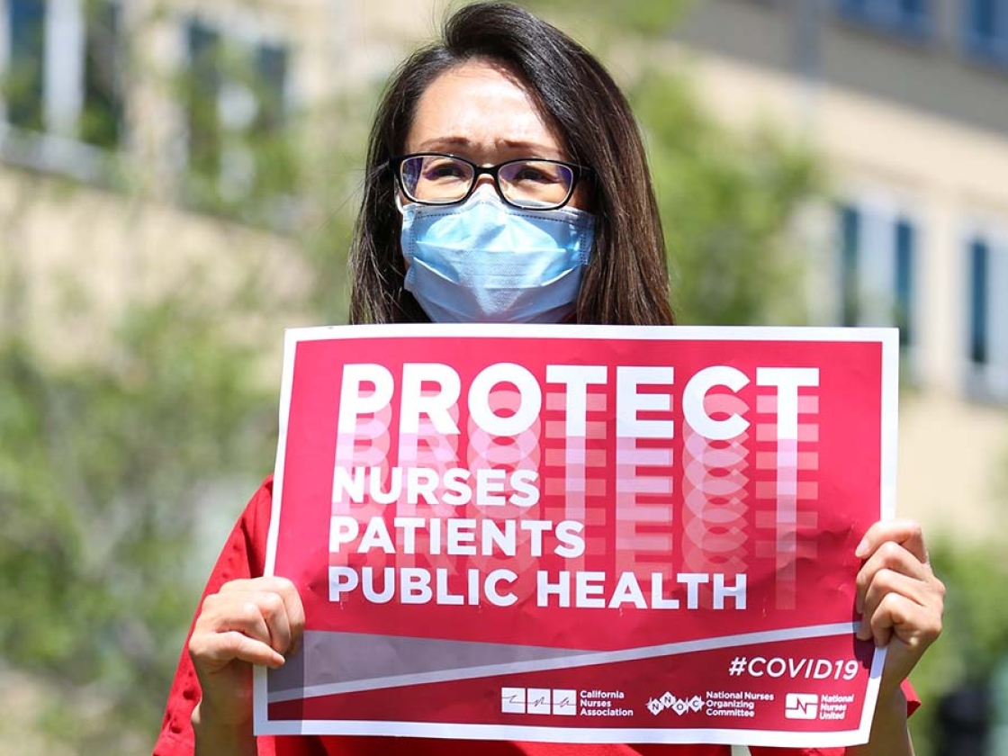 Nurse outside holds sign "Protect Nures, Patients, Public Health"
