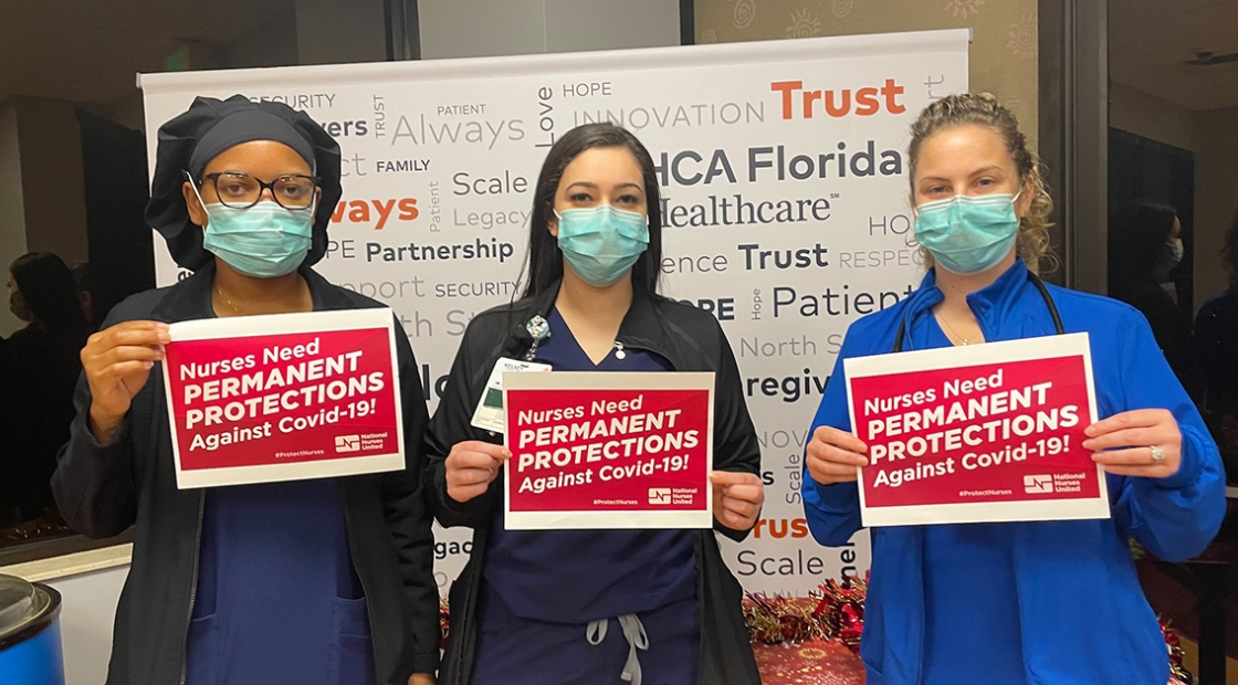 Three nurses hold signs calling on OSHA to enact permanent protections against Covid-19
