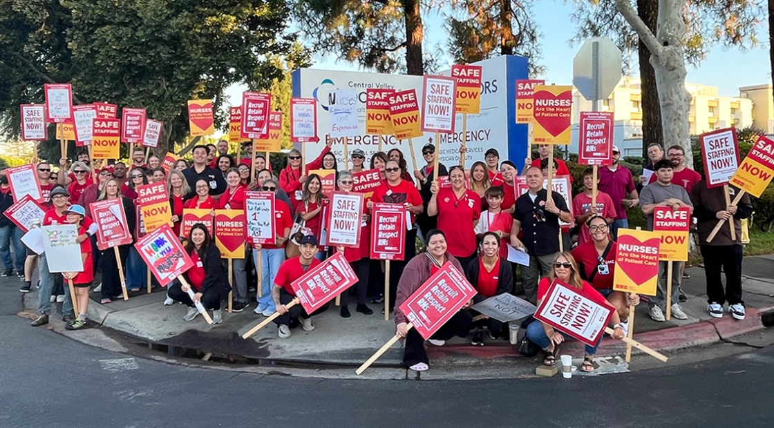 Large group of nurses outside hospital holding signs calling for safe staffing