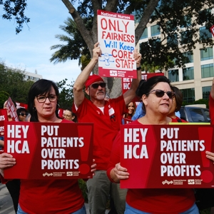Nurses outside hospital picketing, holding signs "Hey HCA, Put Patients Over Profits"