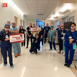 Large group of nurses in hospital hallway, two hold signs "Patients First"