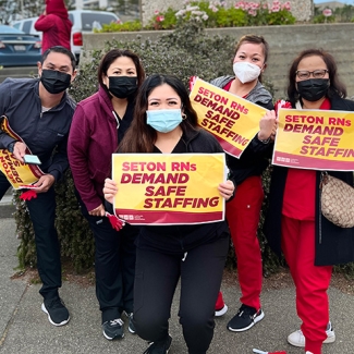 Group of five nurses outside Seton Medical Center, holding signs "Seton RNs Demand Safe Staffing"