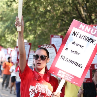 Nurse holding sign "NNU: Newborns deserve a better beginning" and shirt "Patients before profits"