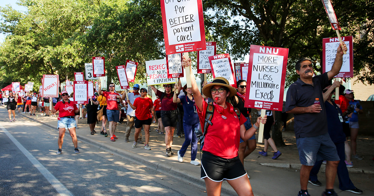 Large picket line of nurses holding various signs