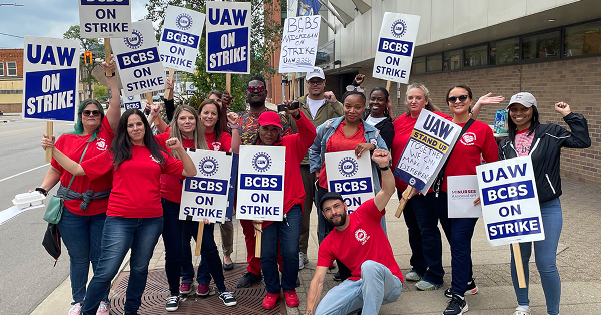 Large group of nurses standing outside holding signs supporting UAW and BCBS workers on strike