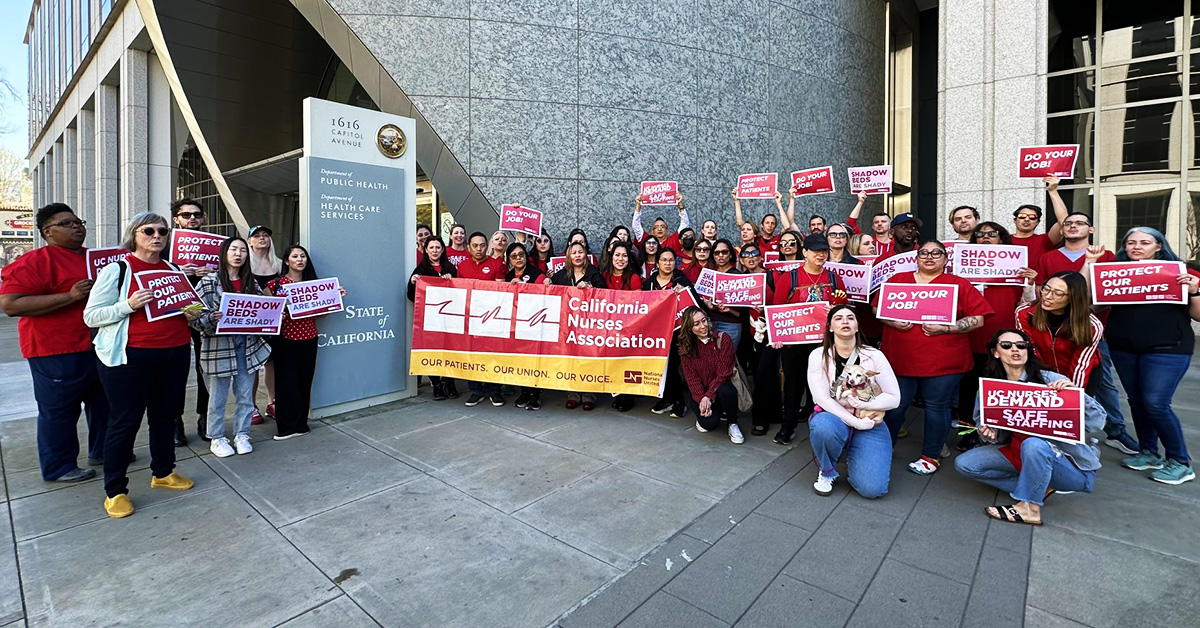 Large group of nurses outside California Department of Public Health building holding CNA banner, signs that say "Protect Our Patients" and "Do You Job"