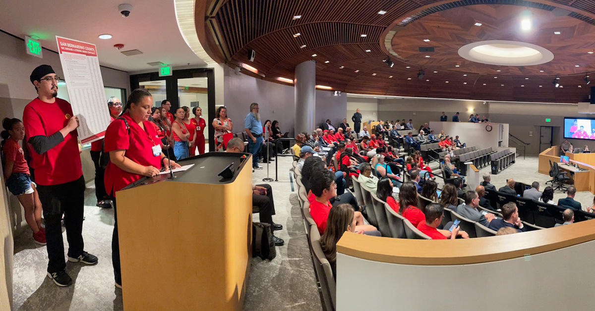 Nurse in red scrubs speaks at podium at board of supervisors meeting