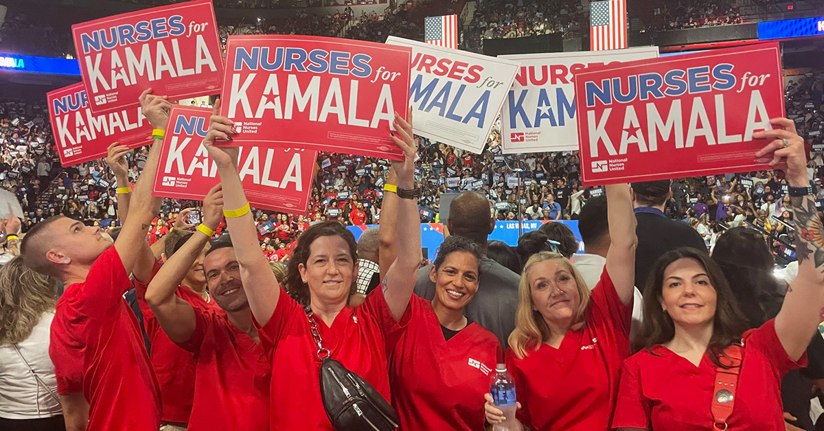 Group of nurses at indoor campaign rally holding signs "Nurses for Kamala"