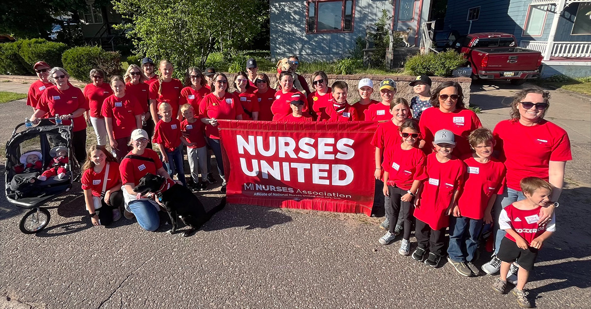 Large group of nurses and family wearing red, holding banner "Nurses United"