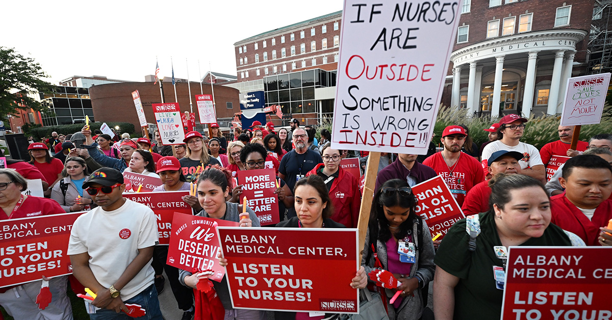 Large crowd of nurses outside hospital holding signs "Albany Medical Center, Listen To Your Nurses" and more