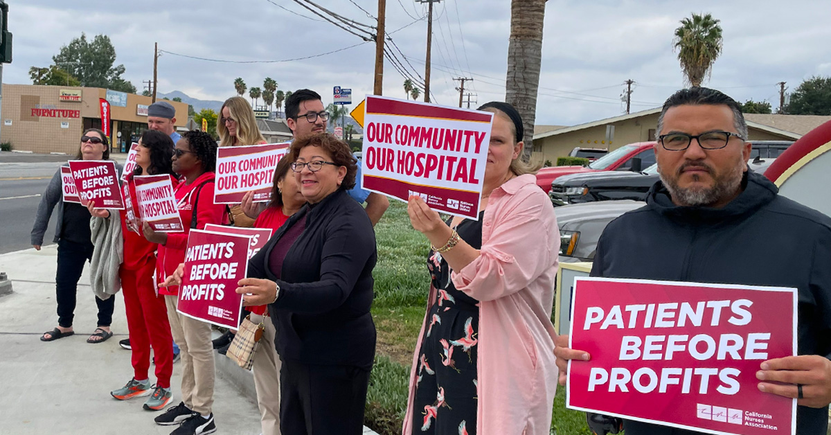 Nurses standing outside holding signs "Patient Before Profits" and "Our Community Our Hospital"