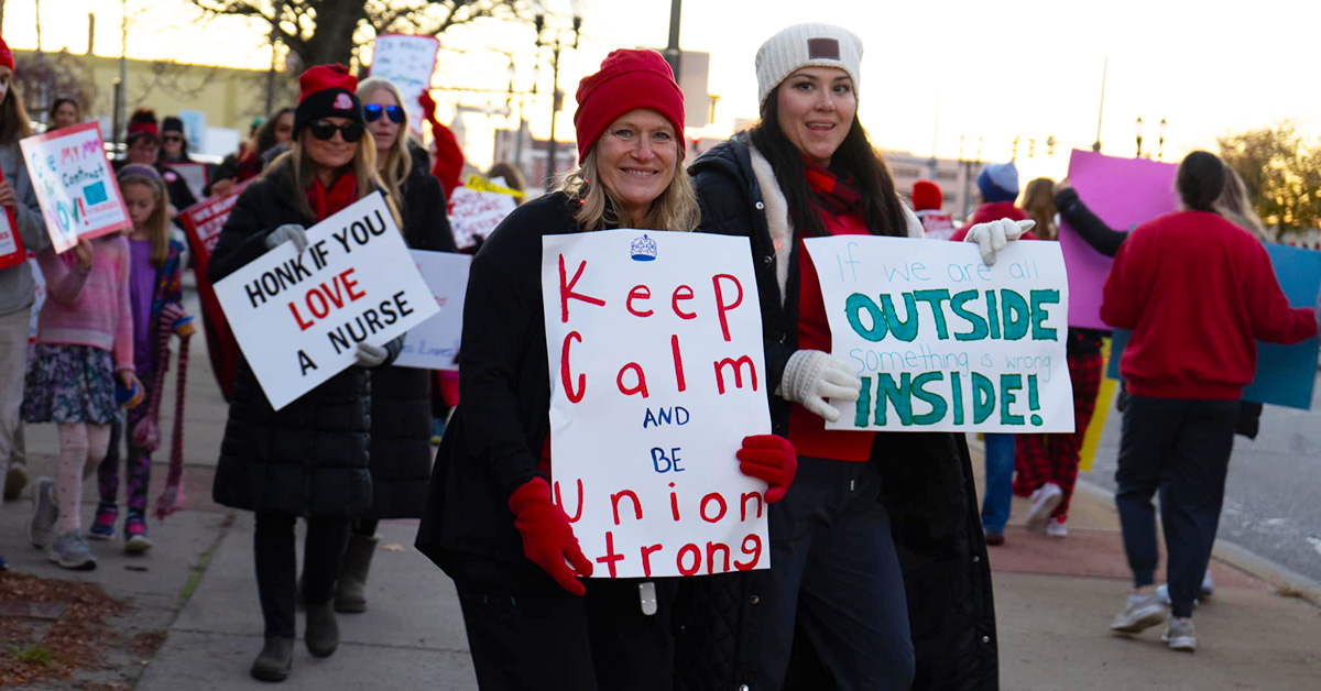 Two nurses, outside, holding signs "Keep Calm and be Union Strong" and "If we are all outside, something is wrong inside"