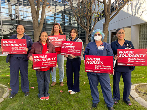 Group of six nurses outside holding signs "Union Nurses Build Healthy Communities"