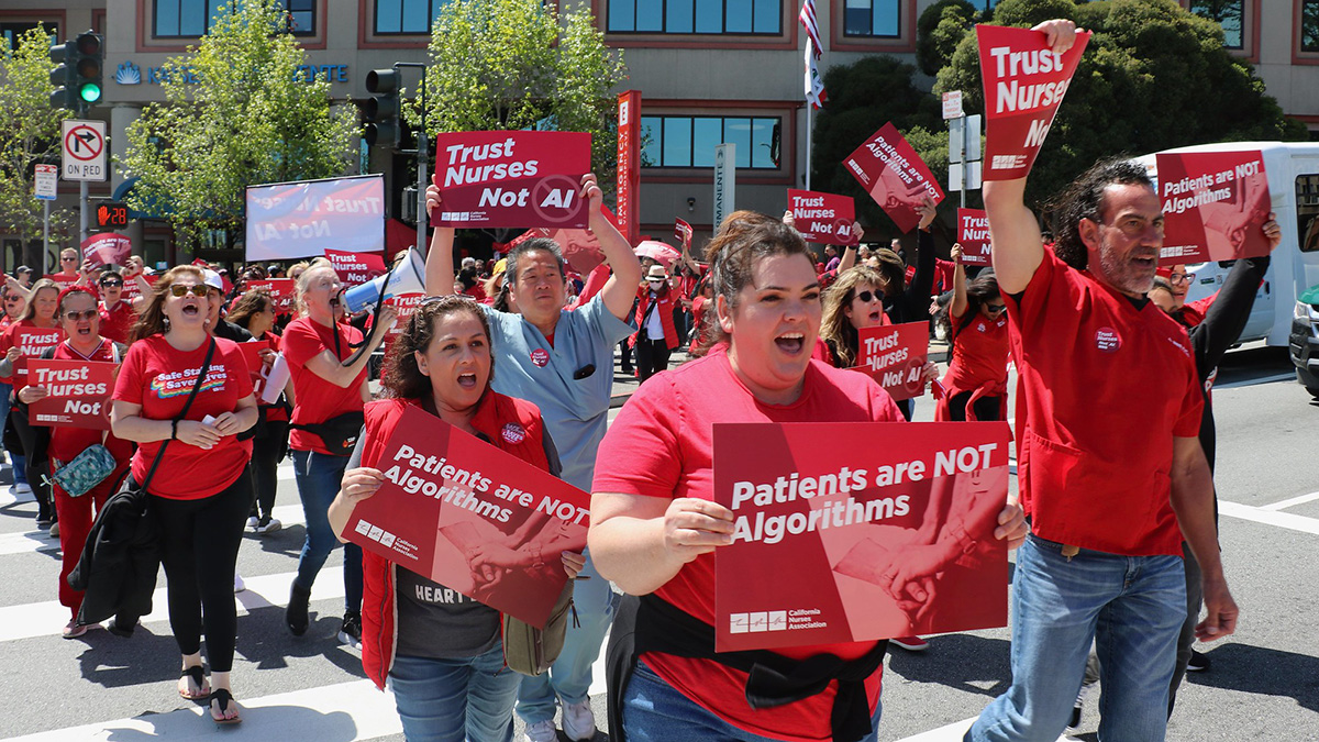 Group of nurses marching holding signs "Patients are Not Algorithms" and "Trust Nurses, Not A.I."