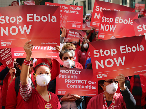 Masked nurses holding signs "Stop Ebola NOW"