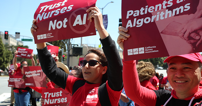 Twonurses outside holding signs "Patients are Not Algorithms" and "Trust Nurses, Not A.I."