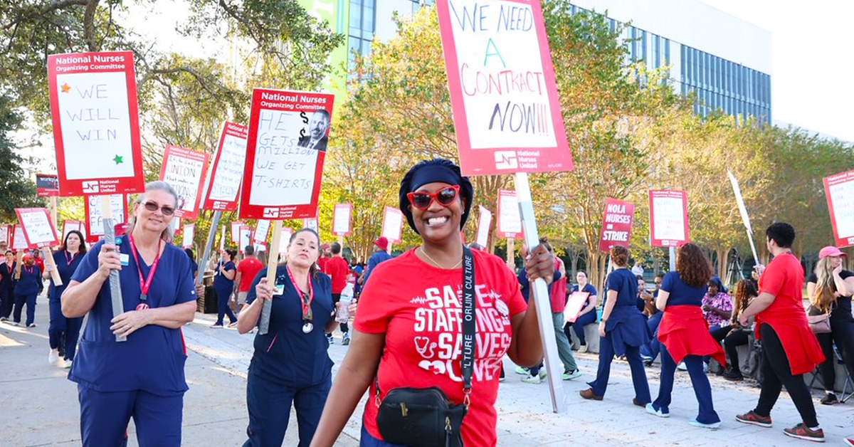 Nurses on picket line outside of hospital, smiling, holding signs about being on strike.