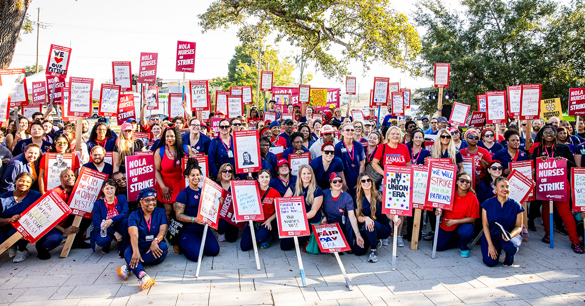 Very large group of nurses grouped outside hospital holding signs about going on strike