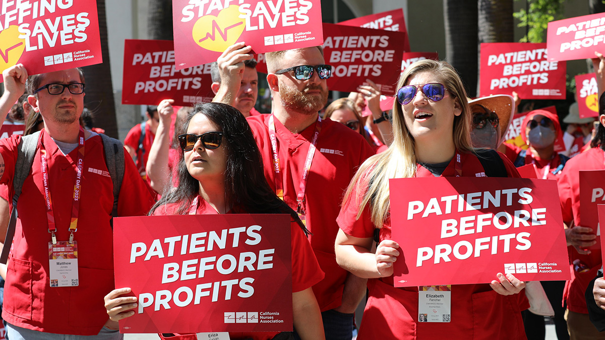 Nurses marching holding signs "Patients Before Profits" and "Safe Staffing Saves Lives"