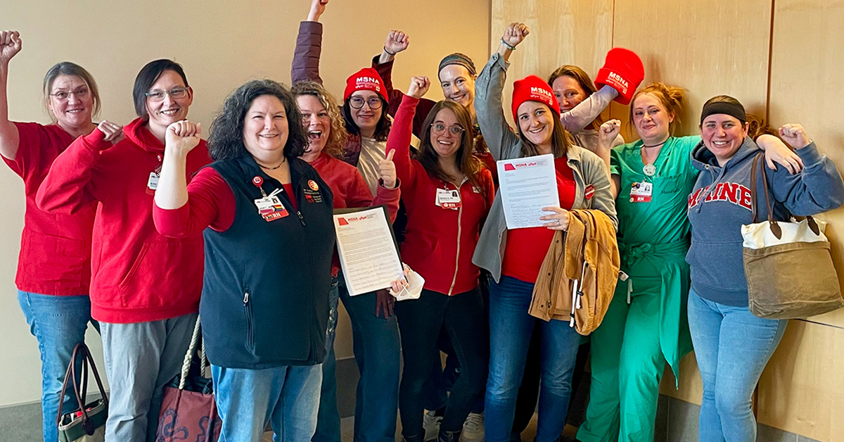 Large group of nurses inside hospital, smiling, with raised fists.