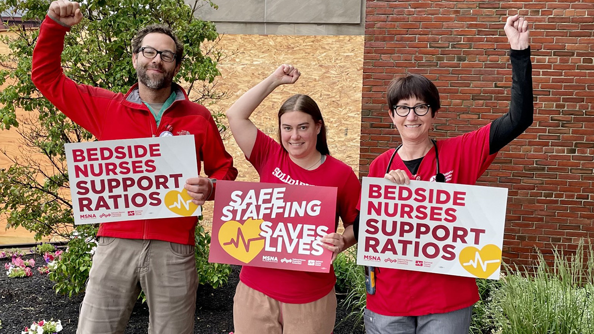 Nurses with raised fists, holding signs "Bedside Nurses Support Ratios"