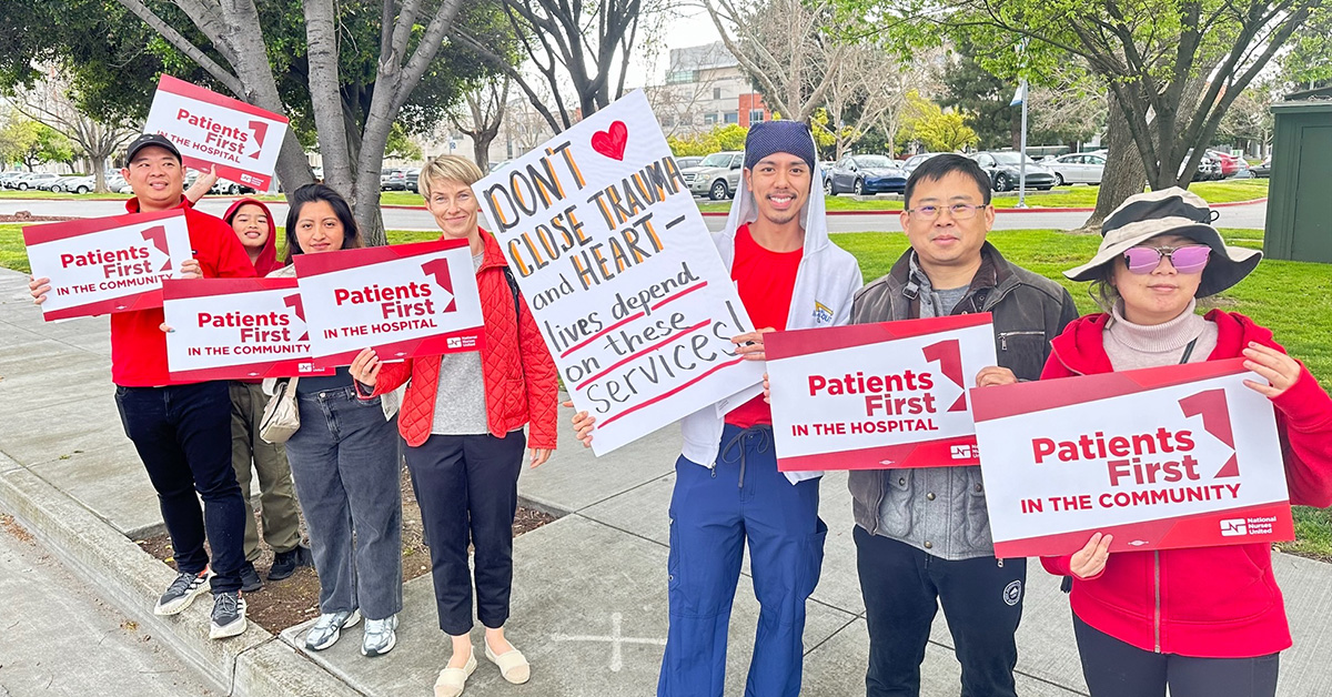 Nurses outside hold signs "Patients First in the Hospital", "Patients First in the Community", and "Don't Close Trauma and Heart"