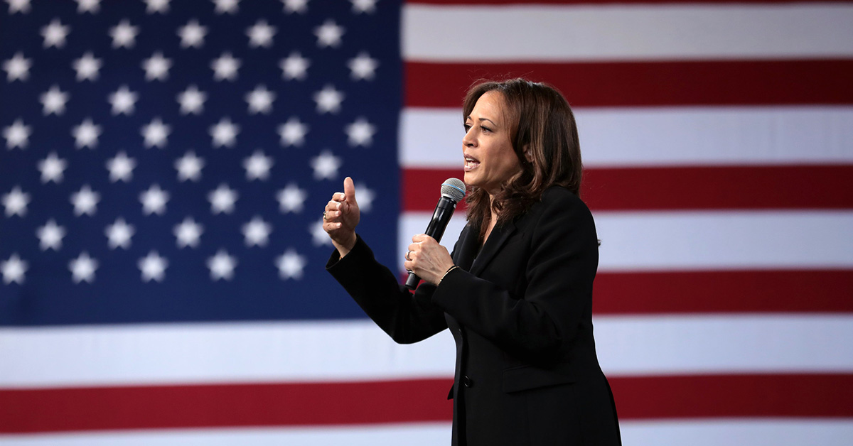 Vice President Kamala Harris speaking into microphone in front of American flag