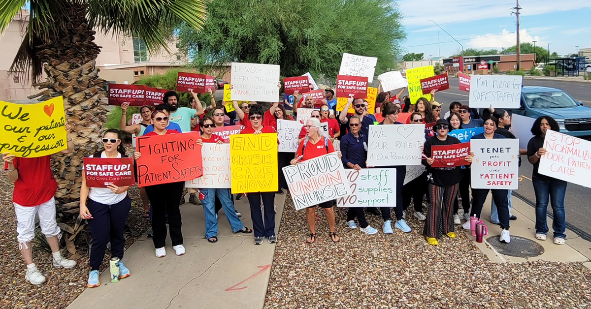 Large group of nurses outside hospital holding signs calling for safe staffing