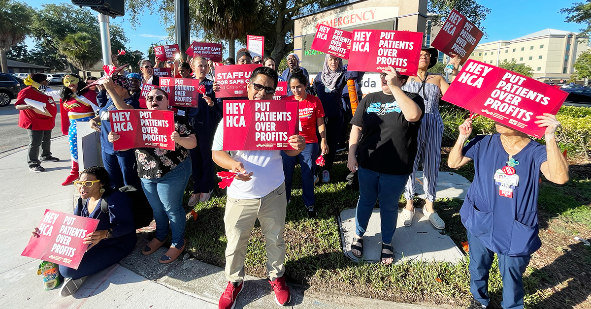 Nurses in from of HCA Florida Osceola Hospital holding signs "Hey HCA, put patients over profits"