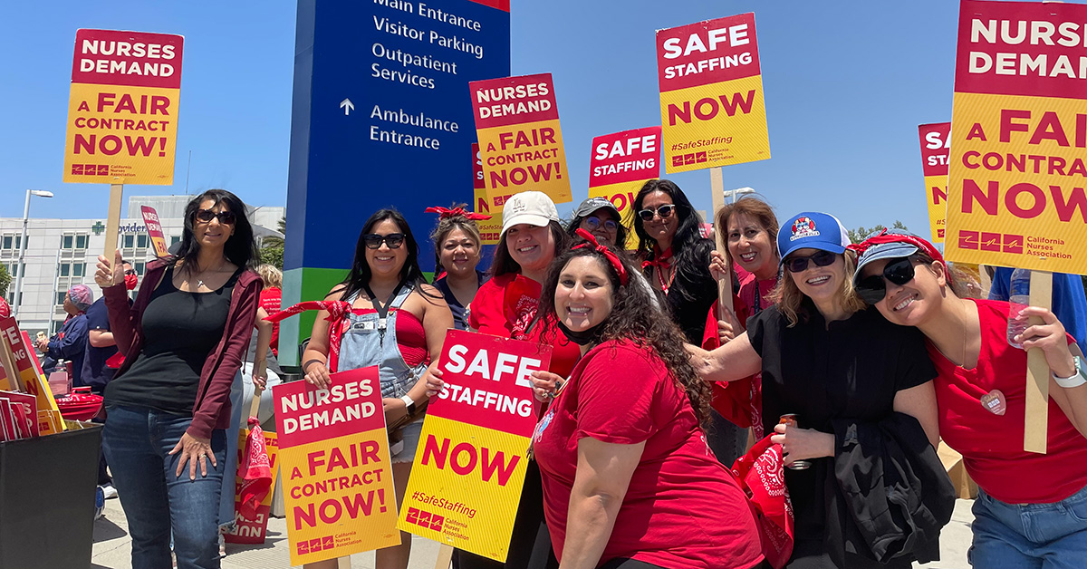 Group of nurses outside Providence Little Company of Mary Medical Center smiling and holding signs "Safe Staffing Now" and "Nurses Demand a Fair Contract Now"