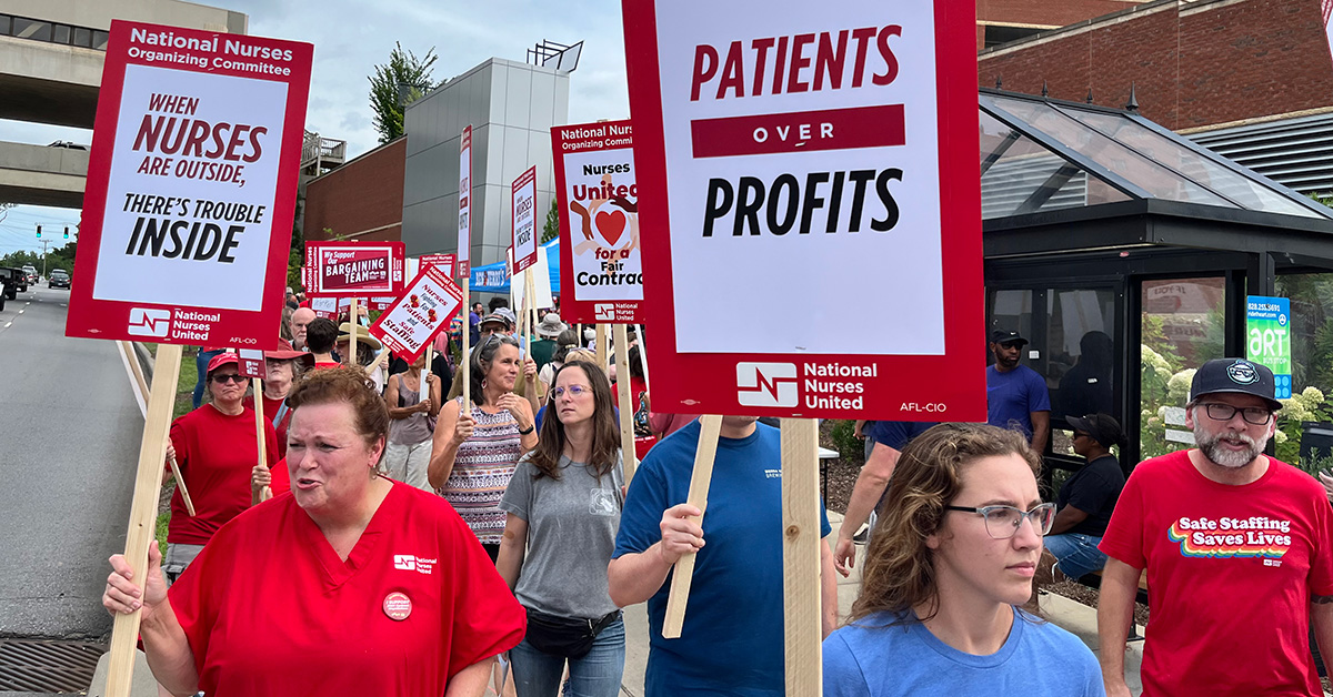 Nurses picketing outside hospital holding signs "Patients over Profits"