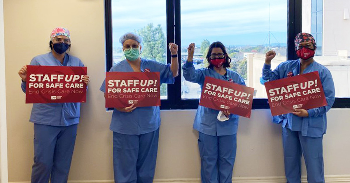 Four nurses inside hospital holding signs "Staff Up for Safe Patient Care"