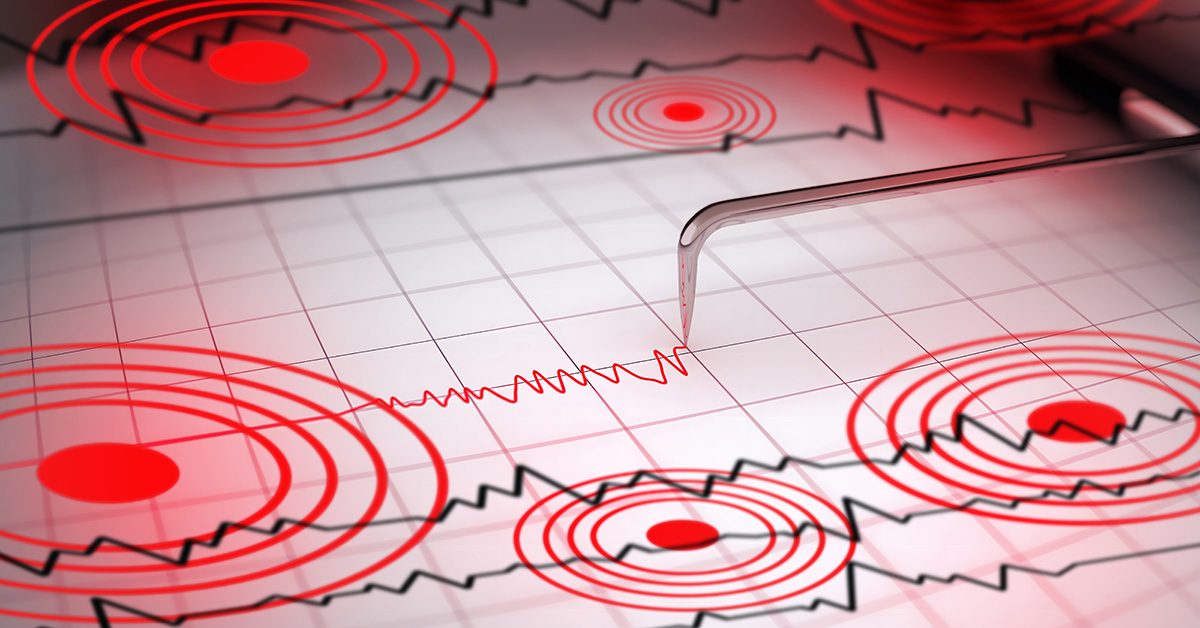 Close-up of a seismograph machine needle tracing seismic waves, indicative of earthquake activity, on graph paper with epicenter rings.