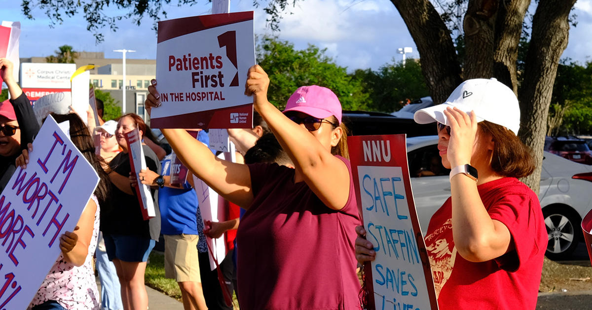 Nurses on picket line, one holds signs "Patients First in the Hospital"