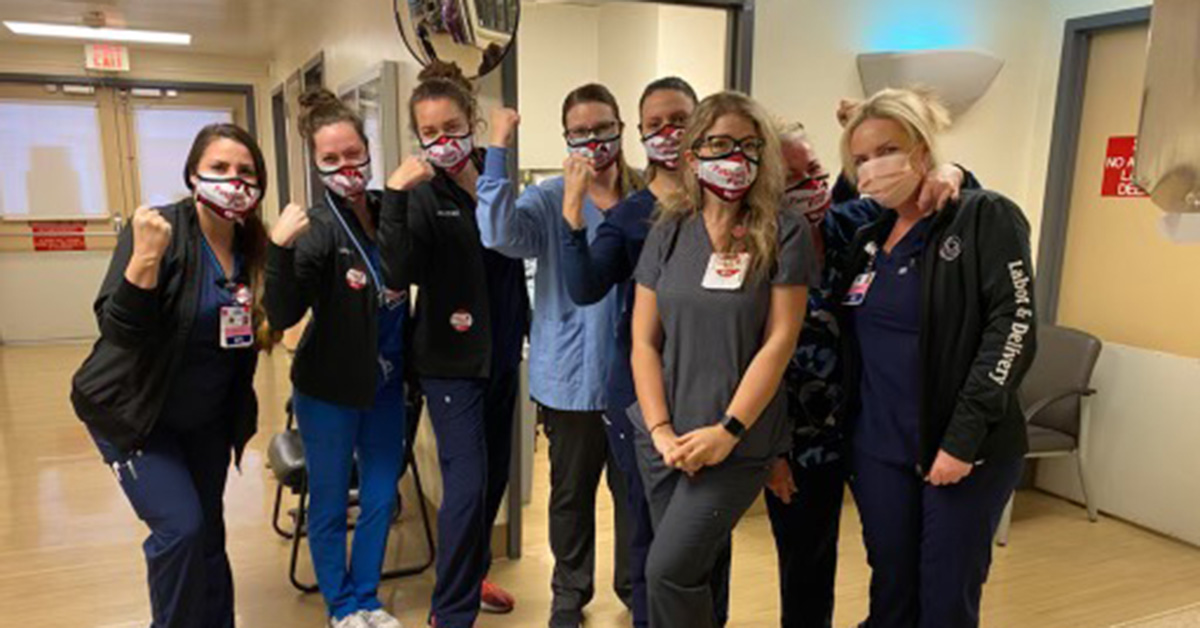 Group of nurses inside hospital, side-by-side, some with raisded arms/fists