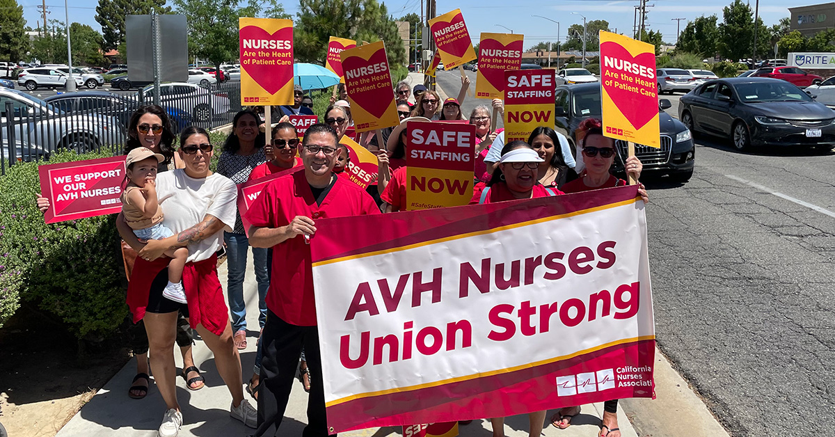 Group of nurses walking outside holding banner "AVH Nurses Union Strong" and signs "Nurses are the heart of patient care"