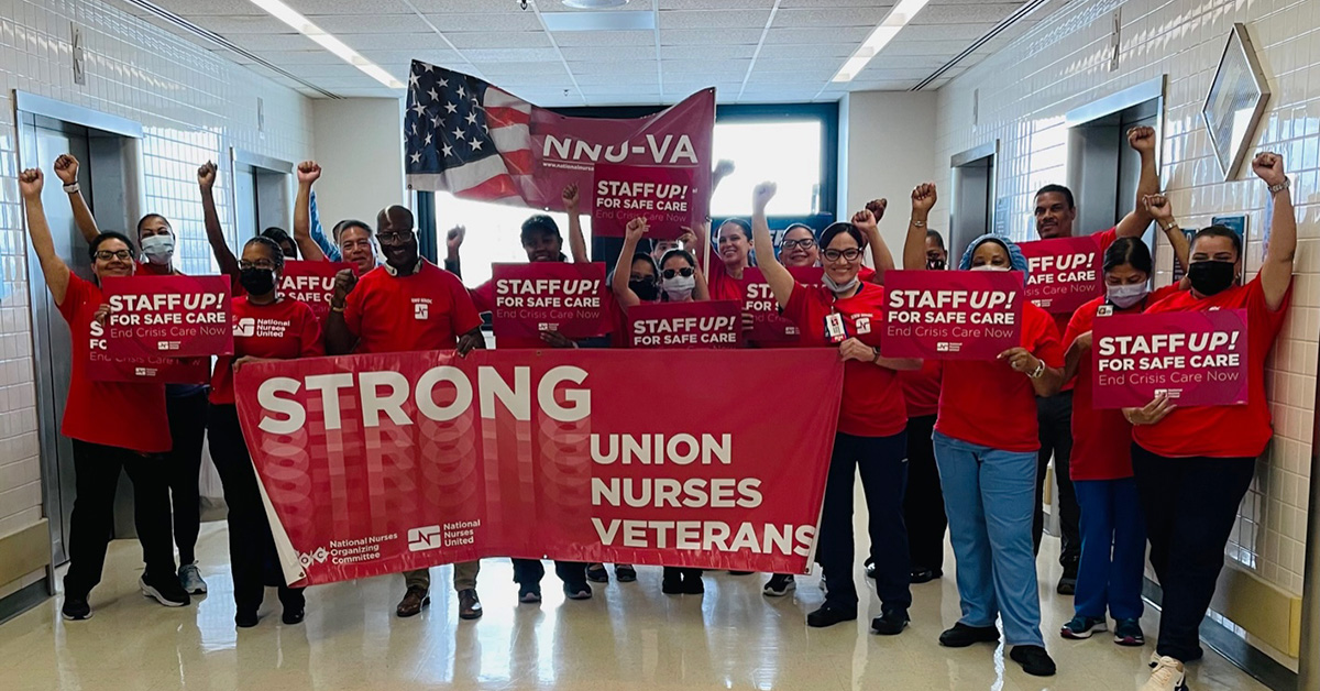 Larg group of nurses inside hospital wearing red, fists raised, holding banner "Strong Union, Strong Nurses, Strong Veterans"