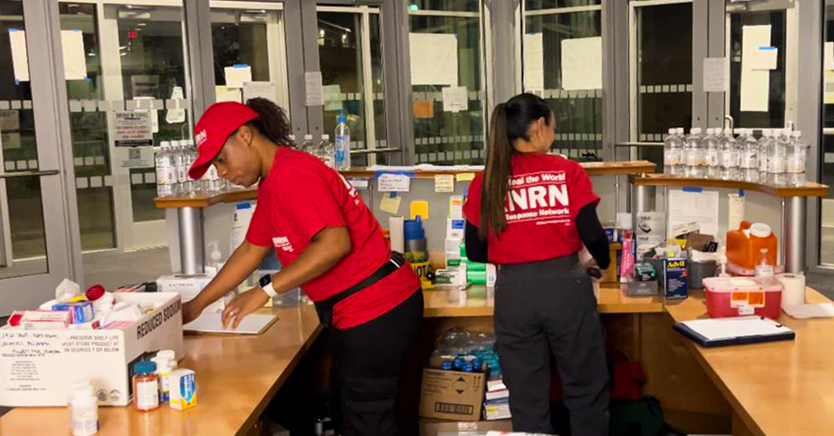 Two nurses inside hospital wearing RNRN shirts and hats preparing clinic