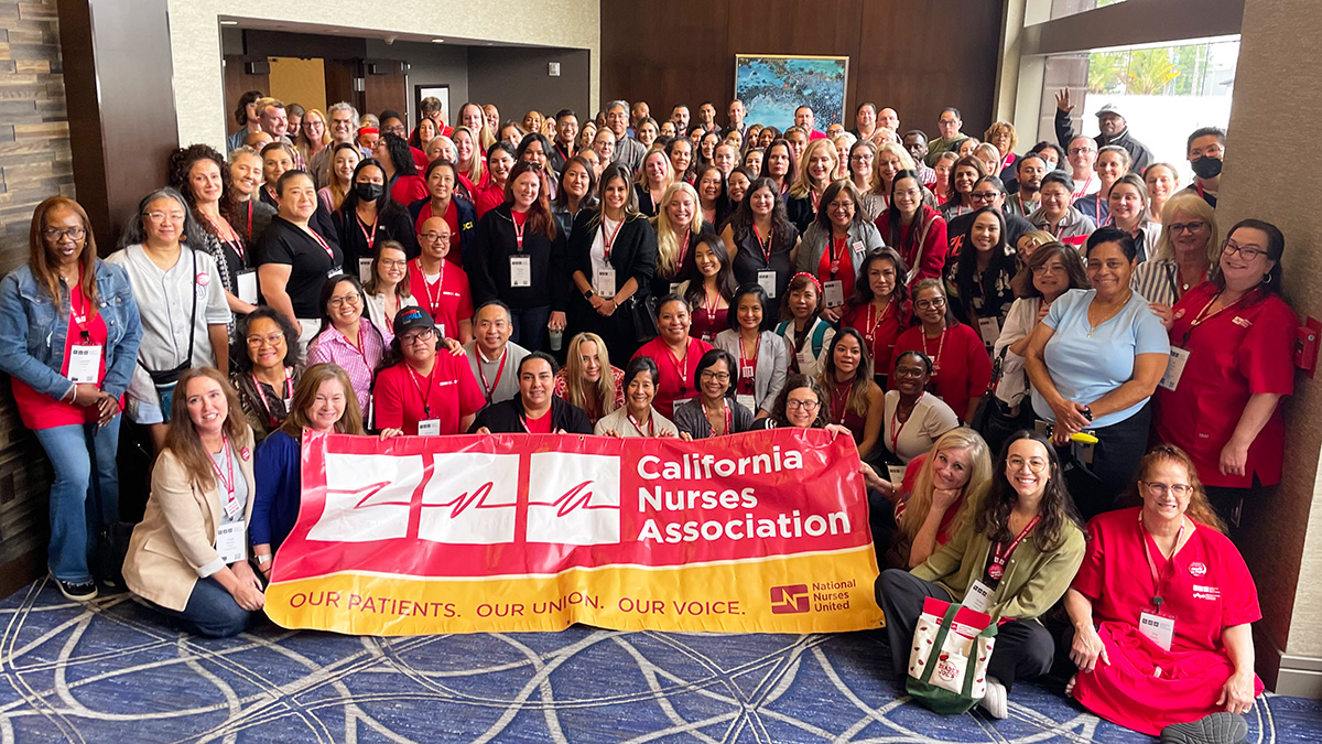 Large group of nurses inside hospital smiling, holding banner "California Nurses Association"