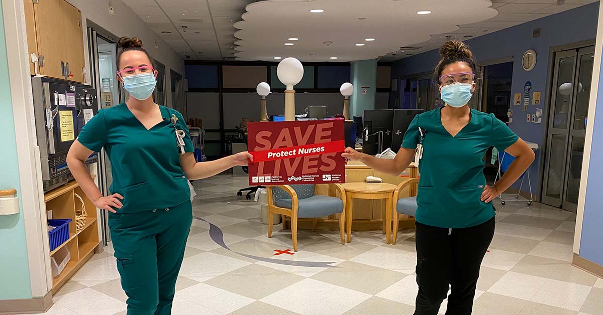 Two nurses inside hospital hold sign "Save Lives: Protect Nurses"