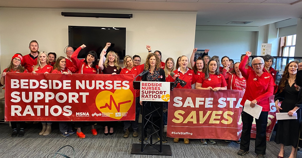 Large group of nurss with raised fists hold banner "Bedside Nurses Support Ratios"