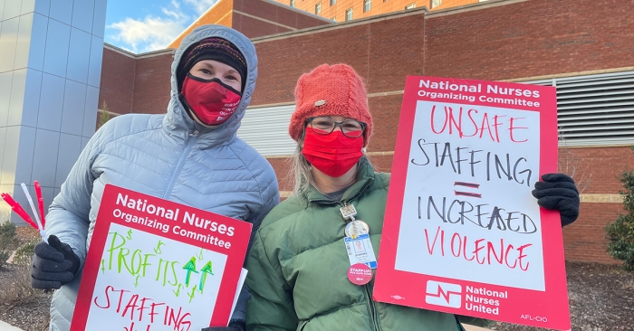 Two nurses outside hospital holding signs calling for workplace safety