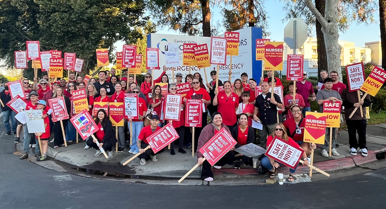 Large group of nurses outside hospital holding signs calling for safe staffing