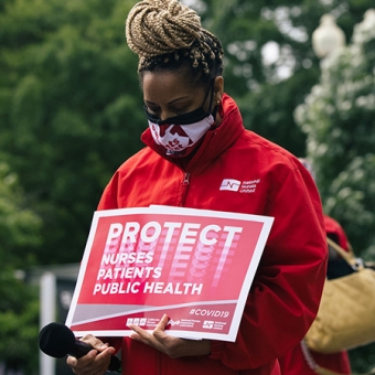 RN with bowed head holding sign "Protect nurses, patients, public health."