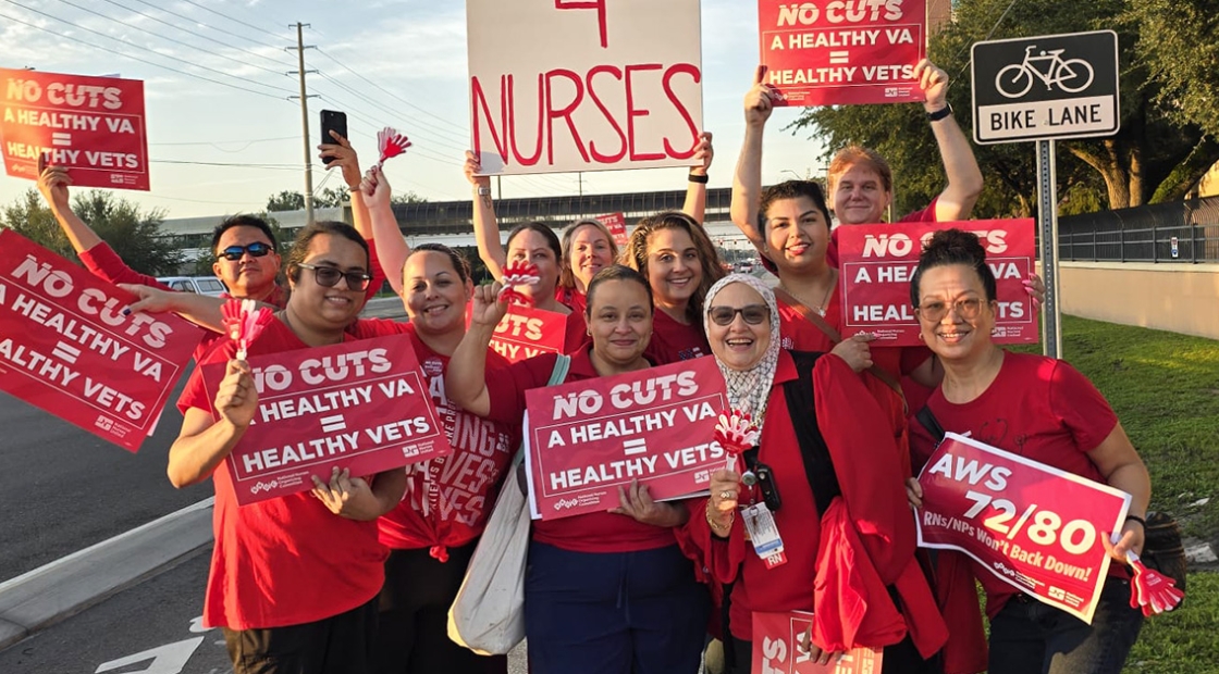 Group of nurses by side of the road smiling, holding signs "No Cuts: A Healthy VA = Healthy Vets"