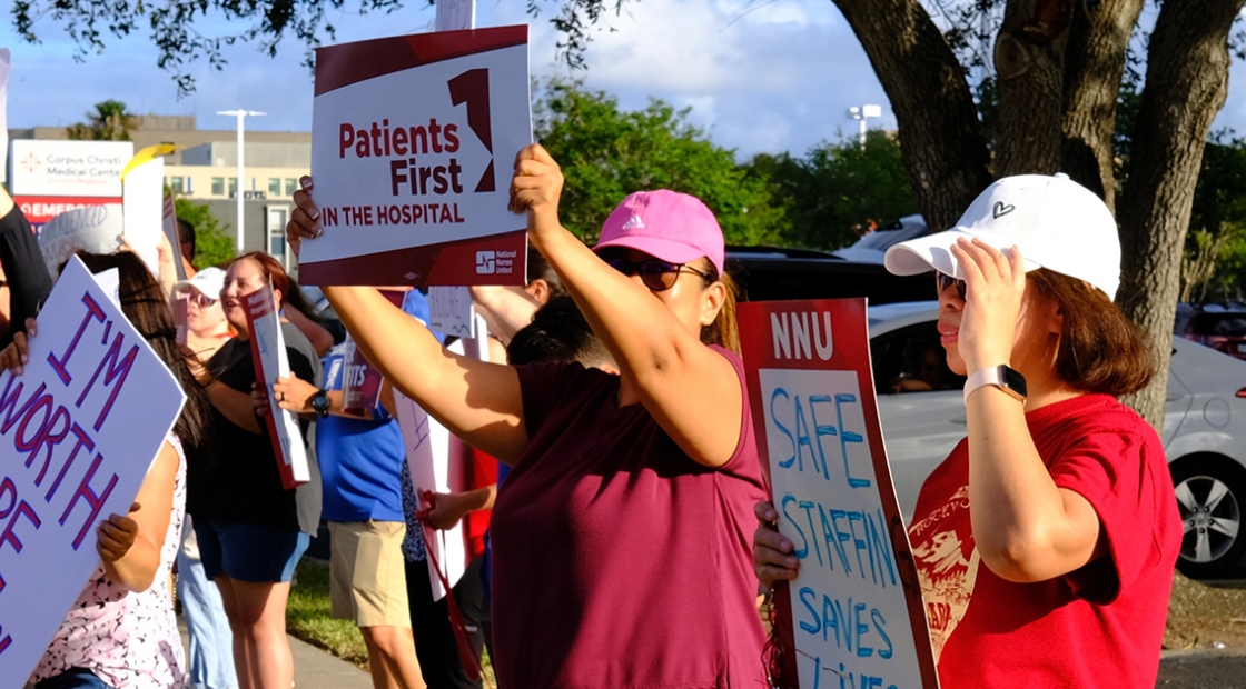 Nurses on picket line, one holds signs "Patients First in the Hospital"