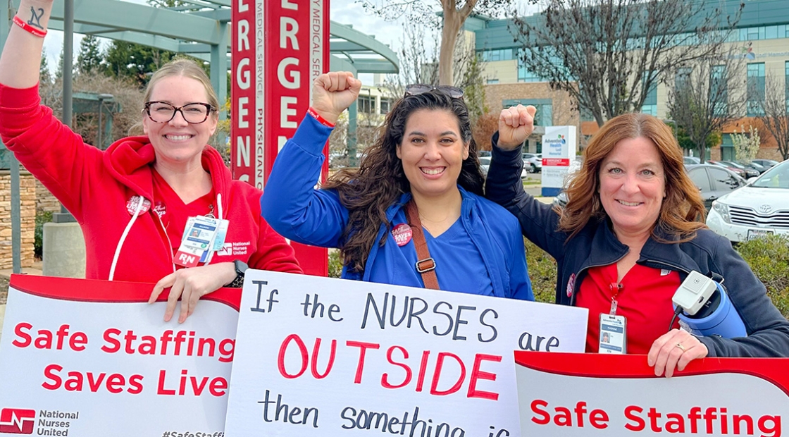 Three nureses outside of hospital, smiling, fists raised, and holding signs "Safe Staffing Saves Lives"