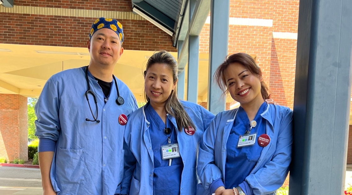 3 nurses in blue scrubs outside standing side-by-side, smiling